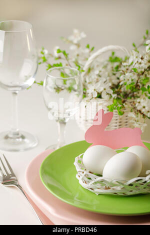 Happy easter. Decor and table setting of the Easter table - Branches of flowering spring tree, dishes of pink and green color. Selective focus. Stock Photo