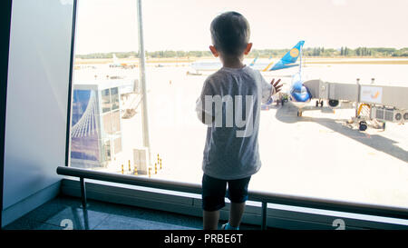 Rear view photo of little boy looking on runway at airport through big window Stock Photo