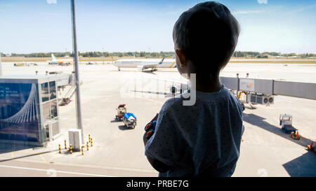 Silhouette of little boy looking on landing airplanes at airport through big window Stock Photo