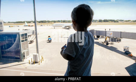 Silhouette of little toddler boy looking on airplanes through big window in airport Stock Photo