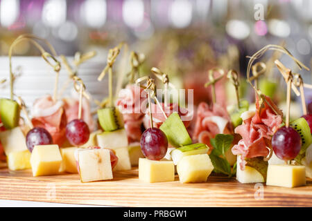 the buffet at the reception. Assortment of canapes on wooden board. Banquet service. catering food, snacks with cheese, jamon, prosciutto and fruit Stock Photo