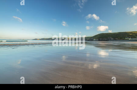Wet sand of scenic beach reflecting morning sky with green cliffs in background. Newgale in West Wales, Pembrokeshire. UK Stock Photo