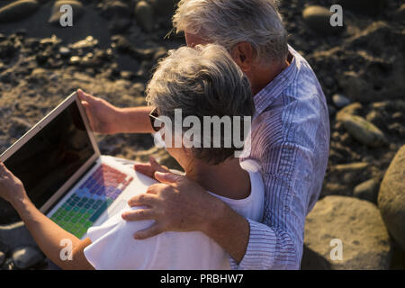 concept of vacation, technology, tourism, travel and people - happy senior couple with tablet pc computer on pebble beach. White hair Stock Photo