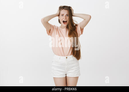 Girl feeling shocked being robbed. Portrait of stunned frustrated young female with cute freckles, holding hands on hair and yelling at camera with amazed expression, being confused and anxious Stock Photo