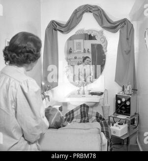 1950s beauty salon. A cosmetologist is treating a client sitting comfortable in a chair. A state of the art electrical device with unknown function is standing on a side table.   Sweden 1950. ref 1519 Stock Photo