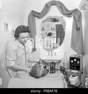 1950s beauty salon. A cosmetologist is treating a clients face with a  state of the art electrical device with unknown function. Sweden 1950. ref 1519 Stock Photo