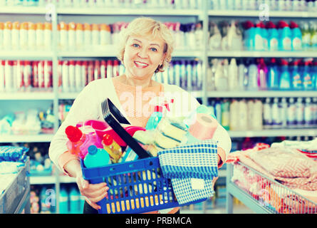 Mature housewife holding basket with chemical products for cleaning home in store Stock Photo
