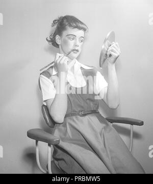 Woman in the 1950s. A young actress is kidding around and putting on theatrical makeup when looking at herself in the reflection of a lid from pot. Sweden 1952. Photo Kristoffersson ref  BD90-9 Stock Photo