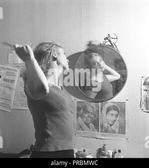 Woman in the 1950s. A young woman is standing in front of a mirror combing her hair. Pictured here swedish actress Ingrid Thulin. 1926-2004. Note how the photographer has positioned her in the mirror so the crack in the Art deco mirror glass, passes through her face. Sweden 1951. Kristoffersson  Ref BB39-12 Stock Photo