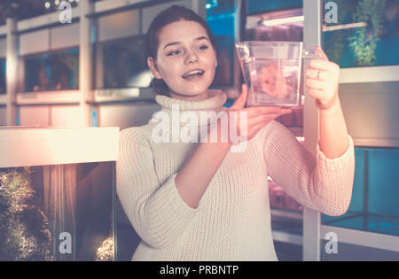 happy russian girl holding plastic container with big colorful fish breed Discus in aquarium shop Stock Photo