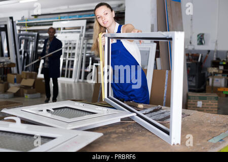 Young female worker manufacturing plastic windows using measuring tape in work Stock Photo