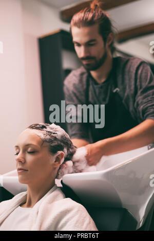 Young woman getting new hairstyle at professional hair styling saloon. Hairdresser is massaging her head. Stock Photo