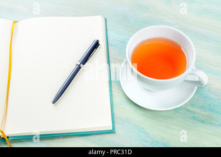 A photo of an open journal with a pen and a cup of tea, shot on a teal blue background Stock Photo