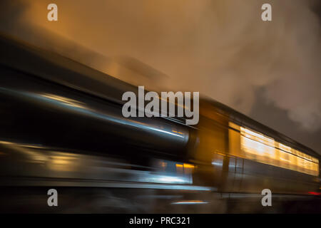 Dramatic, low angle view of moving UK steam train, locomotive at night. Long exposure, movement, motion blur; high speed concept, travelling fast. Stock Photo