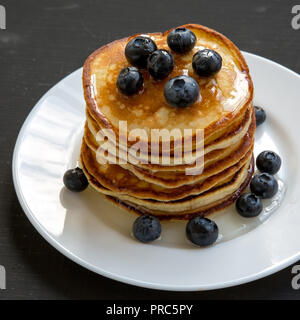 Pancakes with blueberries and honey on white round plate on dark wooden background, side view. Close-up. Stock Photo
