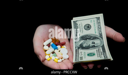 Money and pills in hands, isolated on black. Wasting too much money on medicaments. Drug addiction concept. Stock Photo
