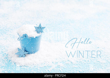 Text Hello winter and little blue pail of snow. Pastel color, snowy greeting card. Winter holidays concept. Stock Photo