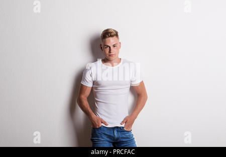 Portrait of a young man in white T-shirt in a studio, hands in pockets. Stock Photo