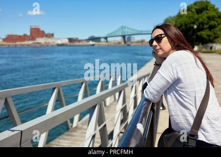 Redhead female with sunglasses watching the scenery of Montreal city and the Saint Lawrence river on a sunny summer day in Quebec, Canada. Stock Photo