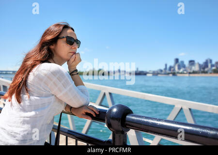 Redhead female with sunglasses watching the scenery of Montreal city and the Saint Lawrence river on a sunny summer day in Quebec, Canada. Stock Photo