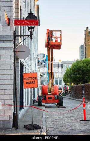 Work lift truck executes construction maintenance on Rue le Royer street and pavement closed (trottoir barre) sign in Montreal, Quebec, Canada Stock Photo
