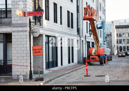 Work lift truck executes construction maintenance on Rue le Royer street and pavement closed (trottoir barre) sign in Montreal, Quebec, Canada Stock Photo