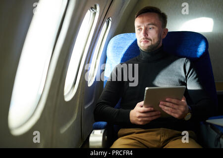 Pensive Man Holding Tablet in Airplane Stock Photo
