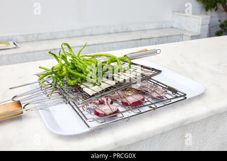 Fresh long green peppers, white cheese and sliced red onions placed between the wire grill grid on a tray over a counter and waiting to get barbecued. Stock Photo