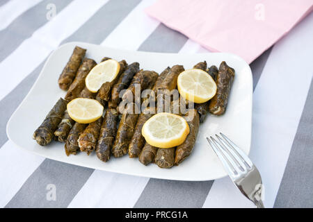 Stuffed grape leaves with olive oil and lemon slices served in a white porcelain plate. Zeytinyagli yaprak dolmasi. Stock Photo