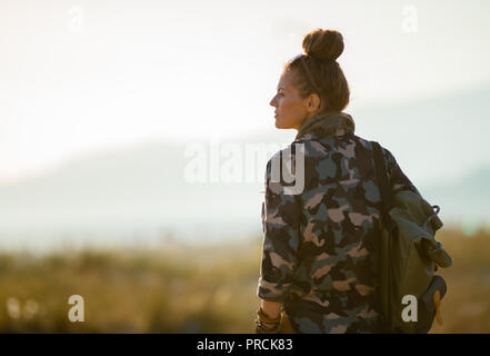 Seen from behind fit traveller woman in hiking gear against mountain and sea landscape at sunset Stock Photo