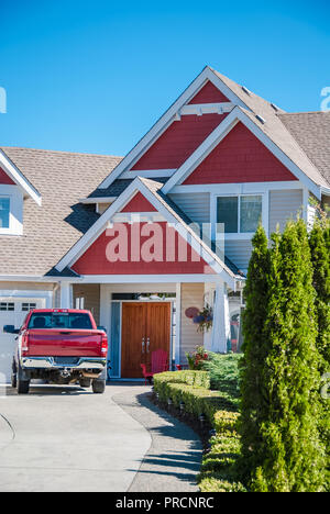 Entrance of luxury residential house with red car parked on the driveway. Red residential house with red truck in front of the entrance Stock Photo