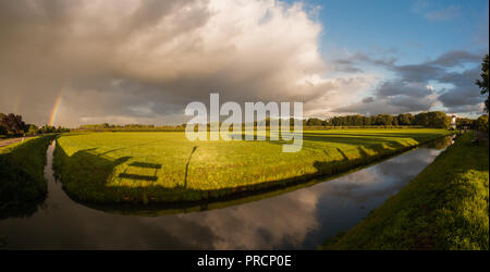 A wide angle shot of a dramatic sunrise with a rainbow reflected in a canal and a traditional dutch windmill in the Netherlands. Stock Photo