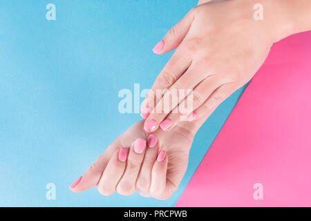 Girl hands with pink nails polish gel on beautiful blue and pink background. Manicure and beauty concept. Close up, top view Stock Photo