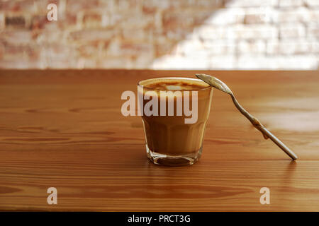 Flat white coffee with spoon on wooden table in cafe. It is espresso-based coffee drink consisting of espresso with microfoam steamed milk with small bubbles with a glossy or velvety consistency. Stock Photo