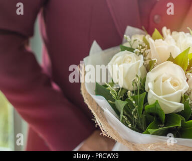Close up groom in red or burgundy wedding suit holding bouquet of white beautiful rose flowers. Stock Photo