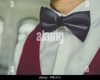 Close-up black bow tie on white clean shirt with red or burgundy vest. Stock Photo