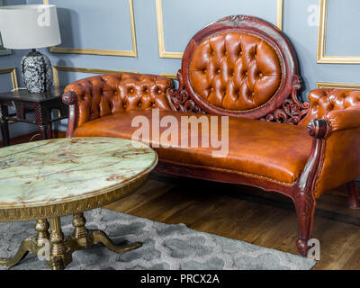 Vintage luxury red brown leather sofa with marble and brass round table and vintage lamp on gray carpet and wooden floor on light blue and golden edge Stock Photo