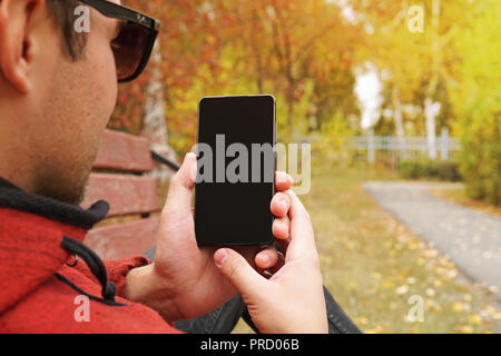 Young man holds in his hand his smartphone and shows the screen. Technology and people. blank black screen for design. use smartphone outdoors in the  Stock Photo