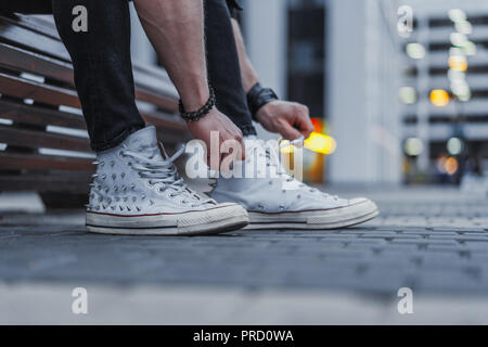 Attractive man tying laces of his white sneakers and sitting on bench. Stock Photo