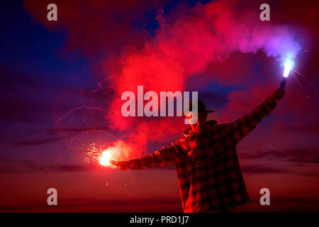 Man stands with signal torches against dark sunset sky Stock Photo