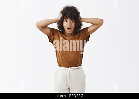 African American woman in trouble starting panic. Portrait of worried insecure and stunned girl with afro hairstyle holding hands on head gasping and opening mouth being in hopeless expression Stock Photo