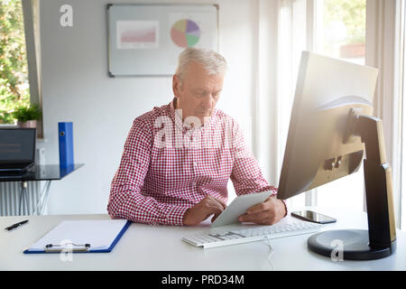 Senior businessman using his digital tablet while sitting at office desk and browsing on the internet. Stock Photo