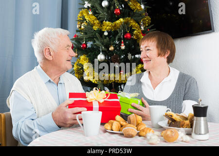 Aged husband and wife exchanging gifts during Christmas at home Stock Photo
