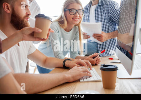 Discussing successful project. Group of young cheerful business people working and communicating while sitting at the office desk together with colleagues sitting in the background. Stock Photo