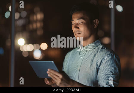 Asian businessman standing in an office at night working online Stock Photo