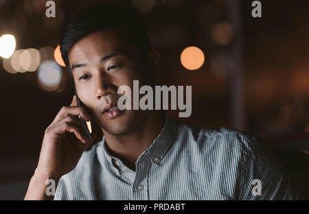 Asian businessman talking on his cellphone in a dark office Stock Photo