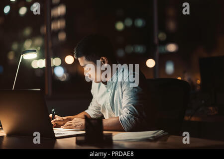 Asian businessman working at his desk late into the evening Stock Photo