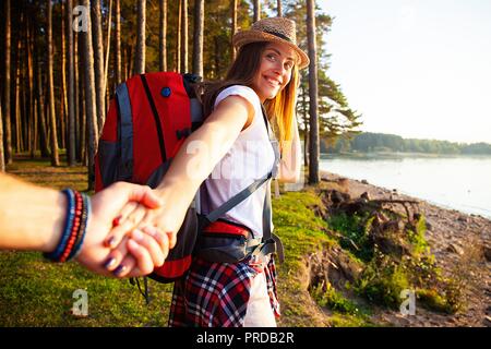 Portrait of happy young woman holding hand of her boyfriend while walking in forest. Stock Photo