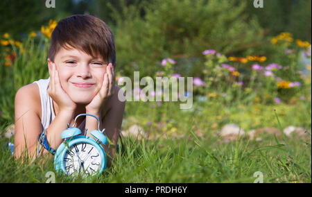 Boy with alarm clock lays in summer garden Stock Photo