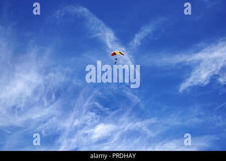 Bright multicolor parachute canopy and skydivers against the background of a blurry white clouds and a blue sky. Tandem master with passenger is flyin Stock Photo